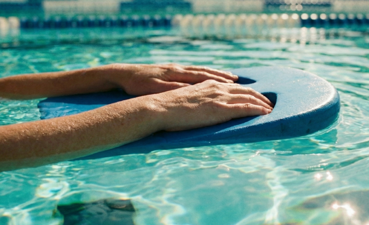 Üben: Nahaufnahme von Händen, die ein Schwimmbrett im Wasser halten – ein Symbol für das aktive Üben der GFK-Schritte.